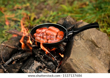 Breakfast of fried eggs and sausages in a pan on a black background.
Kitchen for camping: chicken egg with a bright yolk in a cast-iron skillet near a campfire close-up, breakfast on an open fire.