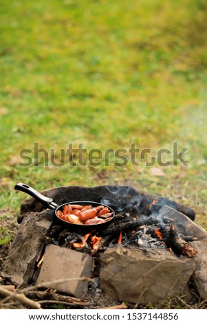 Breakfast of fried eggs and sausages in a pan.
Kitchen for camping: chicken egg with a bright yolk in a cast-iron skillet near a campfire close-up, breakfast on an open fire.Camping food making.