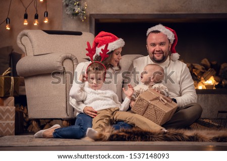 Picture of happy parents in Santa's cap with sons at fireplace with garland in room