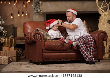 Picture of father in Santa hat and son on red sofa in room