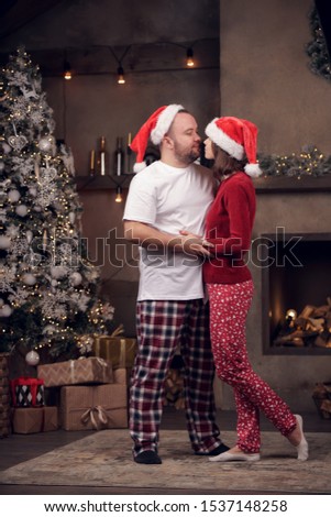 Side picture of embracing men and women in Santa's cap in room