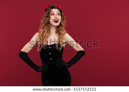 Image of happy cheery woman demon in carnival costume isolated over red wall background looking aside.