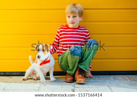 Portrait of happy preteen boy sitting on the ground playing with his clever dog Jack Russell Terrier on yellow background outdoor. Friendship relationship devotion feeling concept.