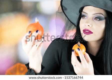 Beautiful young woman dressed in witch costume. Halloween styled muffins on the plate.