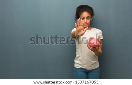 Young black woman putting hand in front. She is holding a piggy bank.