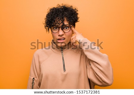 Young mixed african american woman against a brown background showing a disappointment gesture with forefinger.