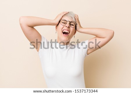 Young authentic natural woman wearing a white shirt laughs joyfully keeping hands on head. Happiness concept.