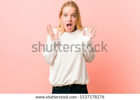 Young blonde teenager woman celebrating a victory or success, he is surprised and shocked.