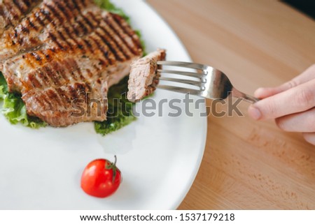Man's hands cutting meat grilled steak with a knife. Salad, cherry tomato and steak on a plate
