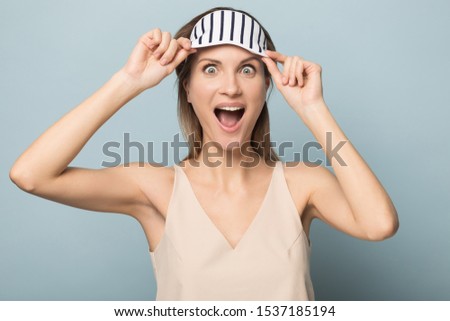 Excited funny Caucasian young woman isolated on blue studio background wakeup peep under striped eye mask relaxed after day sleep, happy millennial female overjoyed with beauty treatment procedure