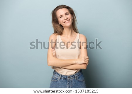 Portrait of smiling confident Caucasian millennial woman isolated on blue studio background posing with arms crossed, happy young female model in casual clothes look at camera shooting casting