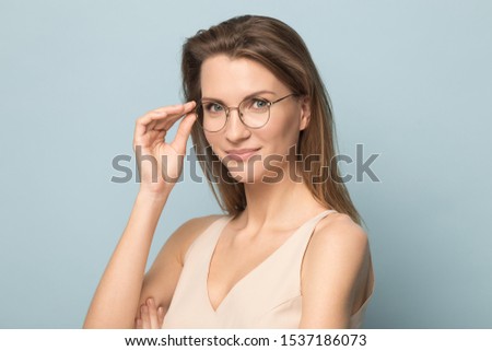 Headshot portrait of beautiful Caucasian woman isolated on blue studio background wear glasses look at camera, millennial female in spectacles posing advertising optician, sight correction treatment