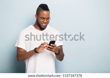 Happy african American millennial male gadget use isolated on blue studio background typing on smartphone, smiling biracial man browsing wireless internet on modern cellphone, blank copy space Royalty-Free Stock Photo #1537187378