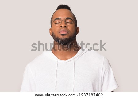 Peaceful african American millennial man in glasses isolated on grey studio background with eyes closed meditating relieve negativity, calm biracial male breathe fresh air, stress free concept