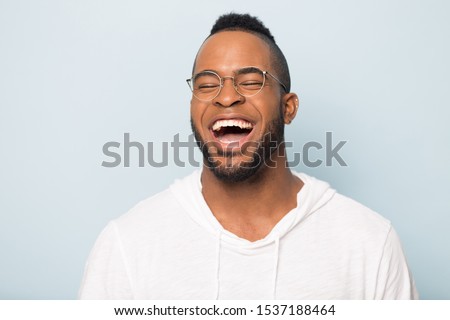 Close up of overjoyed african American millennial man in glasses isolated on blue studio background feel euphoric laugh loud, excited happy biracial male have fun smile at joke, humor concept