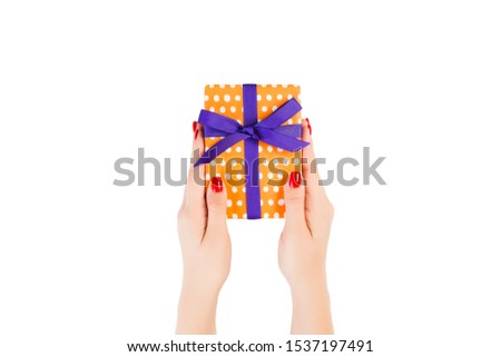 Woman hands give wrapped Christmas or other holiday handmade present in orange paper with purple ribbon. Isolated on white background, top view. thanksgiving Gift box concept.
