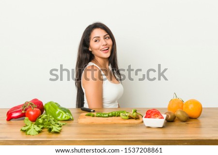 Young curvy woman preparing a healthy meal looks aside smiling, cheerful and pleasant.