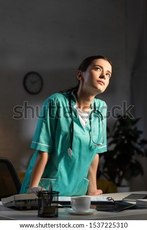 attractive nurse in uniform with stethoscope looking up during night shift