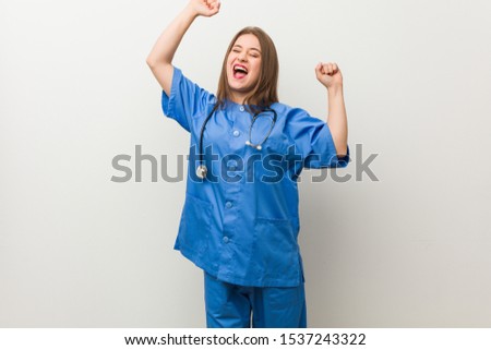Young nurse woman against a white wall celebrating a special day, jumps and raise arms with energy.
