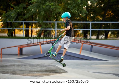 A boy on a scooter and in protective helmet do incredible stunts in skate park. Extreme jump. The concept of a healthy lifestyle and sports leisure Royalty-Free Stock Photo #1537256075