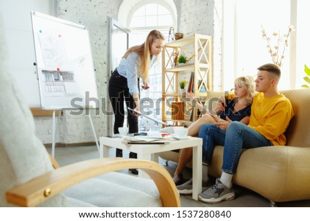 Interior designer working with young couple. Lovely family and professional designer or architector discussing conept of future interior, working with colour palette, room drawings in modern office.