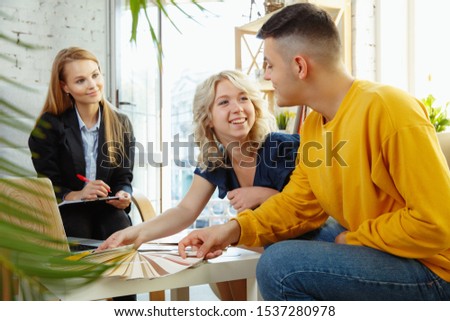 Interior designer working with young couple. Lovely family and professional designer or architector discussing conept of future interior, working with colour palette, room drawings in modern office.