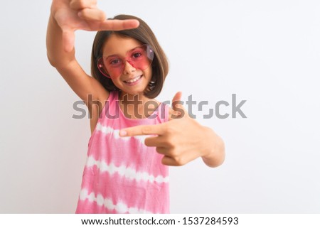 Young beautiful child girl wearing pink t-shirt and sunglasses over isolated white background smiling making frame with hands and fingers with happy face. Creativity and photography concept.