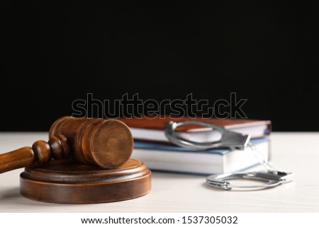 Judge's gavel, handcuffs and books on white table against black background. Criminal law concept