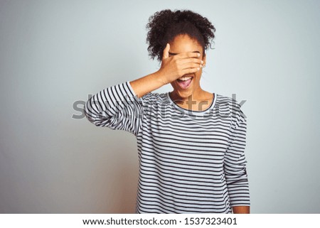 African american woman wearing navy striped t-shirt standing over isolated white background smiling and laughing with hand on face covering eyes for surprise. Blind concept.