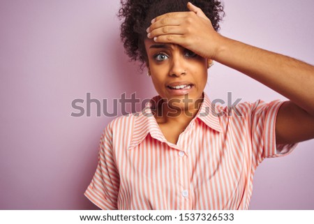 African american woman wearing casual striped shirt standing over isolated pink background stressed with hand on head, shocked with shame and surprise face, angry and frustrated. Fear and upset