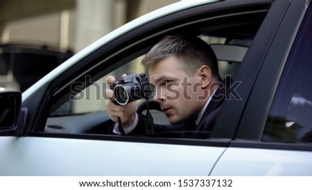 Male agent secretly taking photo by camera sitting in car, photojournalism