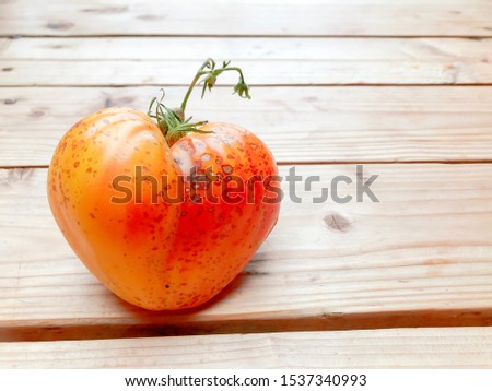 close up of beautiful tomato in a heart form in orange color but have a sickness problem in the skin, isolated on wooden background.  