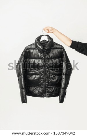 Girl hand holds black jacket on hanger isolated on white background. Minimal fashion clothes concept.