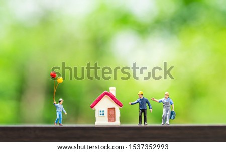 selective focus of miniature worker and tiny home model  on wooden floor over blurred garden background ,macro photography concept idea for solution of property management service.