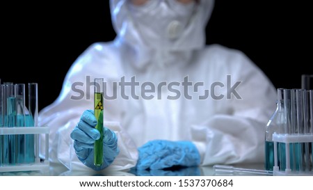 Toxic laboratory worker holding test tube with green ionizing radiation liquid