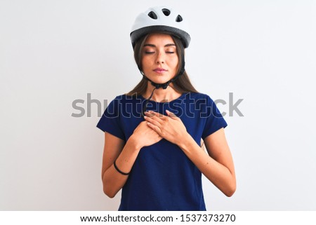 Young beautiful cyclist woman wearing security bike helmet over isolated white background smiling with hands on chest with closed eyes and grateful gesture on face. Health concept.