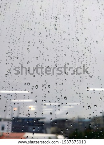 Raindrops on a window pane against a blurry city-space. Rainy day out of the window. Water droplets on the glass background. Blur building background. Pictures of raindrops on glass and the background