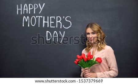 Woman with flowers standing near signature Happy mothers day, congratulations