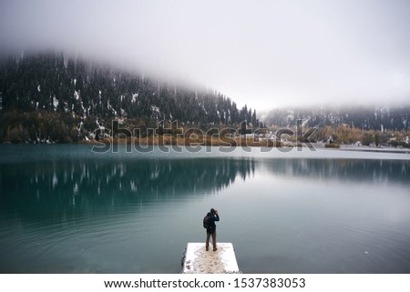 Travel photographer man with backpack standing on the lake wooden pier at mountain lake Issyk, Almaty, Kazakhstan