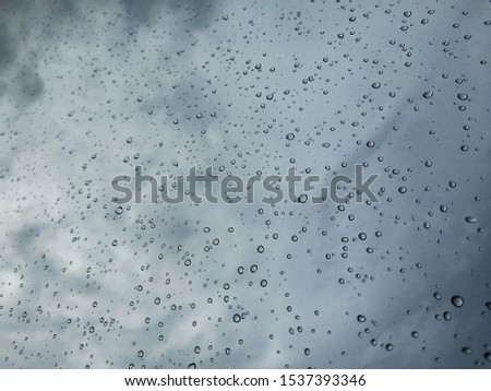 Pictures of raindrops on glass and the background, Rain water droplets with houses in background in City with dark clouds. Rain water droplets on Glass during Rain, dark clouds and detailed water drop