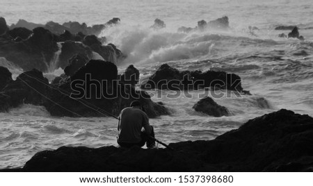 
Angler sitting on volcanic rock by the sea.Picture in black and white