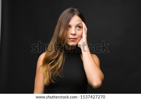 young pretty woman feeling bored, frustrated and sleepy after a tiresome, dull and tedious task, holding face with hand against black wall