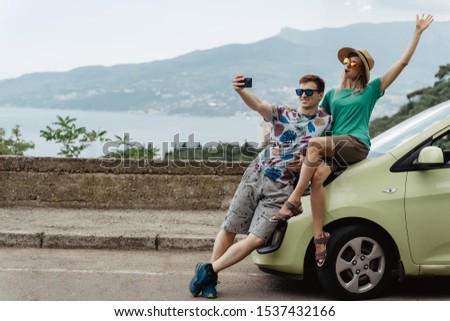 Young man and woman taking selfie on smartphone while travel by car.