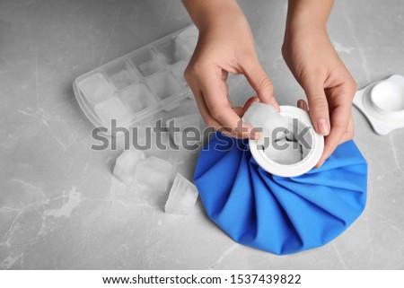 Woman putting ice cubes into pack at marble table, closeup Royalty-Free Stock Photo #1537439822