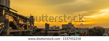 Cityscape picture of Skytrain station and buildings at twilight with clouds in the sky in golden hour from Bangkok Thailand, panoramic web banner