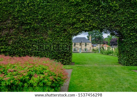 View of a traditional building through the opening in a long bush fence at the Royal Botanic Garden in Edinburgh, Scotland