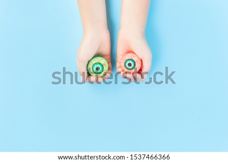 Happy Halloween two bloody eyes in kids hands on pastel blue background. Flat lay banner with copy space. Trick or treat