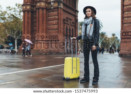 Photographer tourist with retro photo camera. Girl in hat with suitcase travels in Triumphal arch Barcelona. Holiday concept in europe street. Traveler hipster shoot architecture city