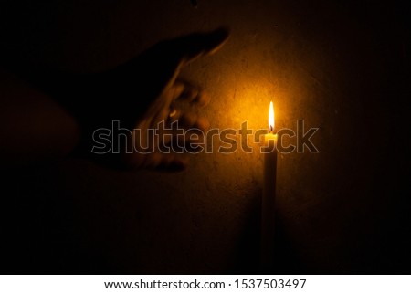 The hand approaching the candlelight in the dark background And there is space for text