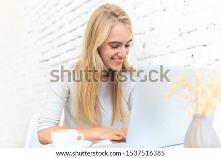 Freelance. Beautiful girl student working and resting in a bright coffee shop with laptop and books . Emotions of joy and smile.